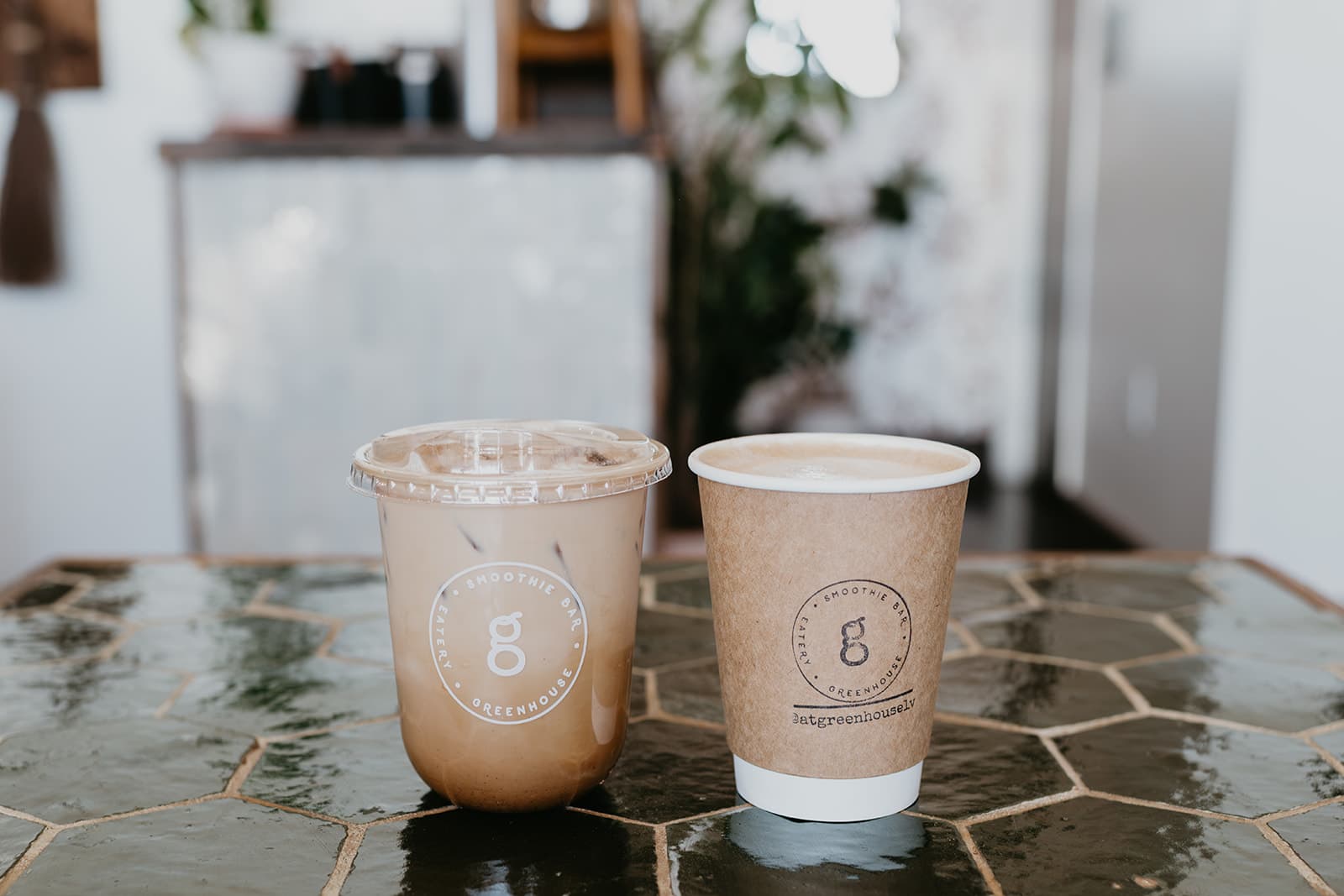 An iced drink and a hot cup side by side on the green tile counter